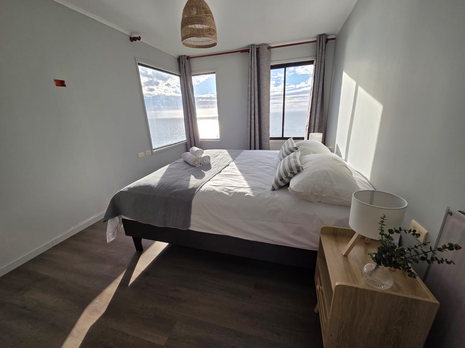 Habitación con cama matrimonial, ventanas al mar y detalles en madera